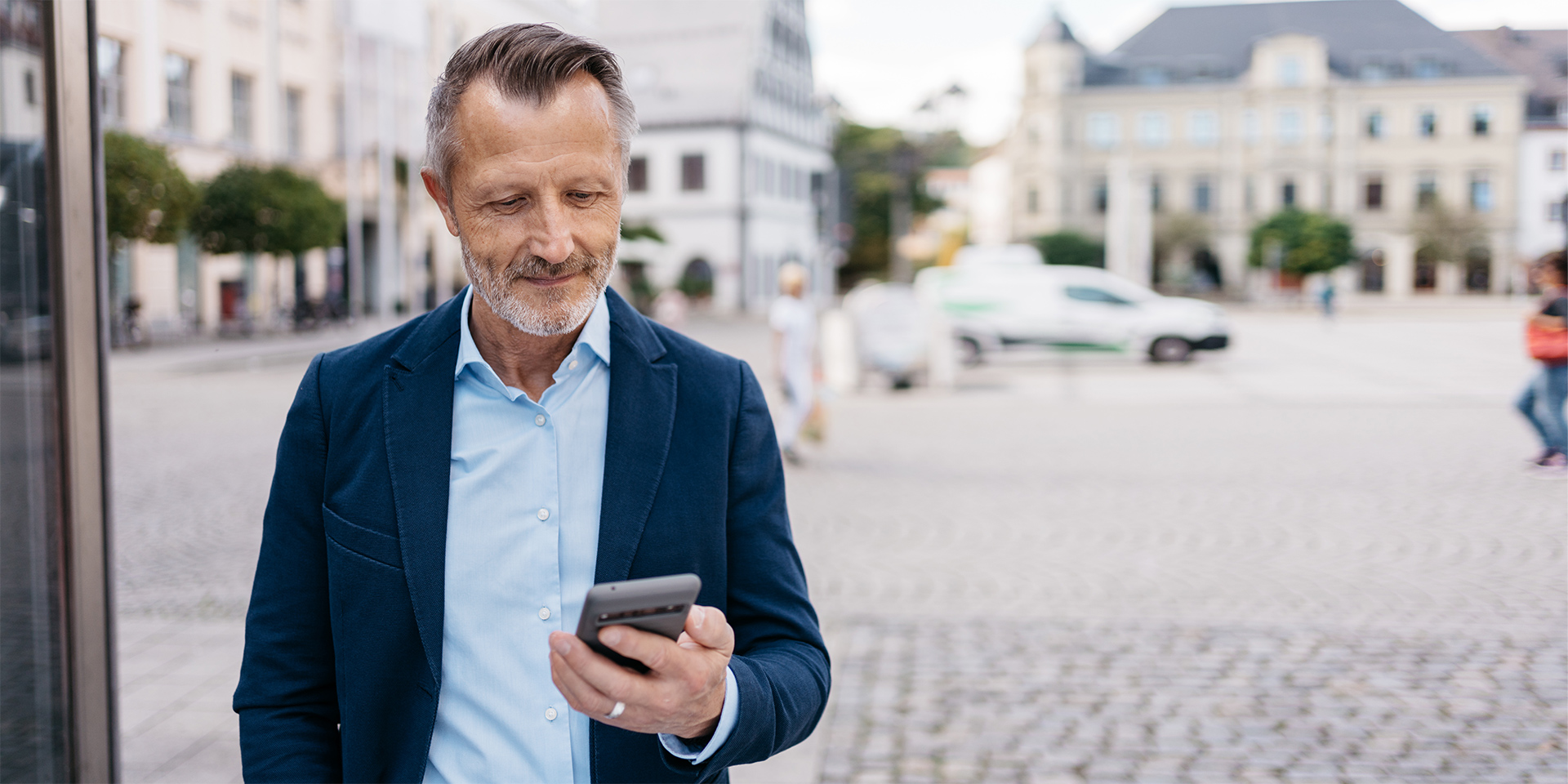 Mężczyzna na tle zabudowy staromiejskiej przedłuża czas parkowania za pomocą aplikacji Mobilet na swoim smartfonie