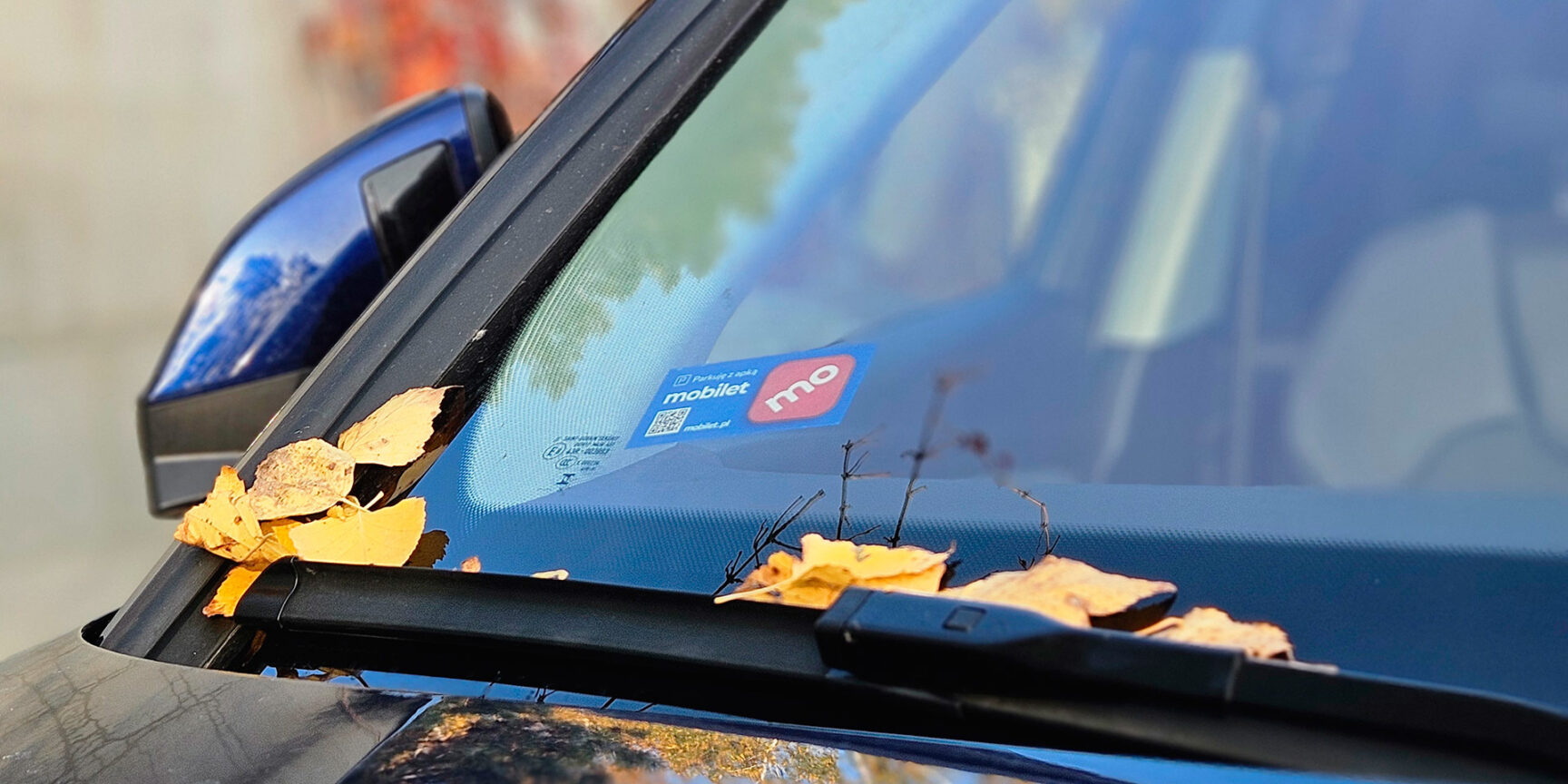 Przednia szyba zaparkowanego samochodu z widoczną naklejką, czyli winietą Mobilet.
