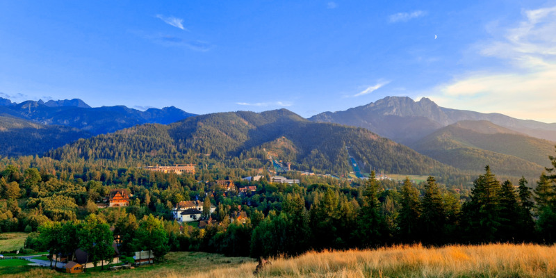 Widok z Antałówki na Tatry, Giewont i skocznie w Zakopanem, gdzie dzięki aplikacji Mobilet kupisz online bilety na autobus i zapłacisz za parkowanie.